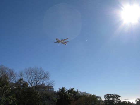 Low Angle View of Small Aircraft Flying over Hillside Homes in Large Blue Sky with Bright Sun