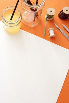 Blank white canvas paper with copy space under spools, knife, brushes and paint on the top edge