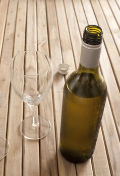 Opened unlabelled bottle of white wine left standing to breath standing on a wooden table with two empty wine glasses, with copyspace