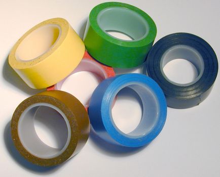 Pile of assorted rolls of electrical insulation tape in different colors over a white background viewed from above