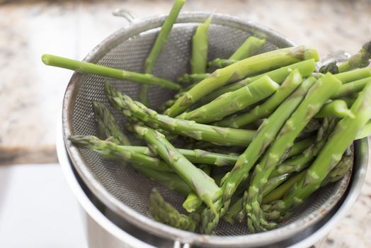 Blanched fresh seasonal green asparagus spears draining in a metal sieve in the kitchen