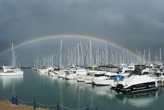 a rainbow and dark storm clouds over yachts in a marina