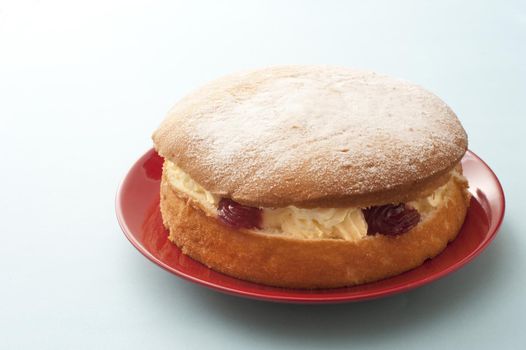 Delicious single little round victoria sandwich sponge cake filled with cream and fruit on red plate over white table