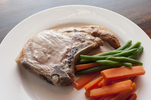 Close-up of roasted pork chop and vegetables on plate