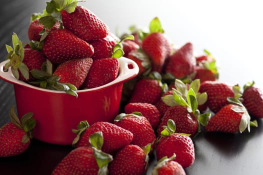 Freshly picked harvest of delicious ripe red juicy strawberries with green stalks overflowing from a small red bowl