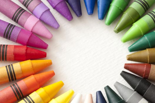 Frame of colorful wax crayons with their points facing inwards in a radiating circle with central blank white copy space