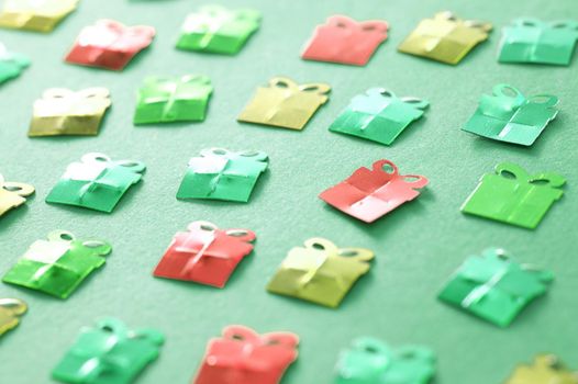 Christmas gift background with paper decorations in the shape of small gift-wrapped boxes scattered across a green surface viewed at an oblique angle