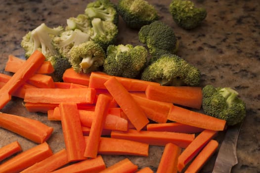 Chopped vegetables on a kitchen counter including carrot batons and broccoli pieces ready to be cooked as accompaniments to a meal