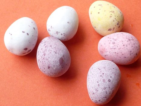 Mini sugar-coated candy Easter eggs in pastel colors to resemble quail eggs scattered on an orange background for the holiday season