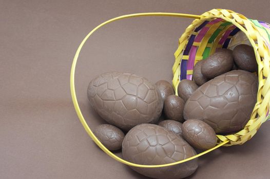 Basketful of chocolate Easter Eggs lying on its side with several eggs spilling out onto the brown background
