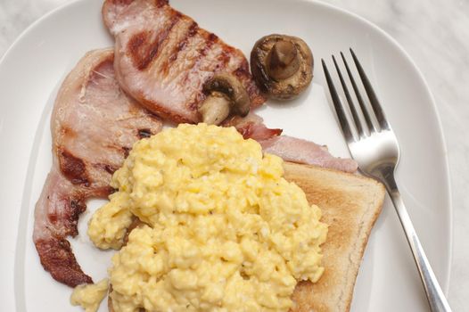 Scrambled egg on toast served with lean grilled bacon rashers and mushroom , close up view from above