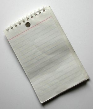Blank spiral bound notepad with ruled lines lying diagonally on a white background