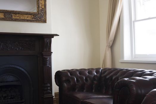 Comfortable leather armchair in a study or living room placed below a window with beige curtain