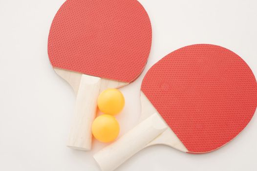 Set of table tennis equipment with two red wooden ping pong bats and two yellow balls on a white background, overhead view with copy space