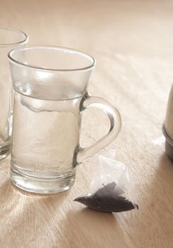 Close Up of Tea Bag on Wooden Table Next to Glass Mugs Filled with Hot Water - Getting Ready to Brew Tea
