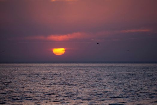 an orange red glowing sunset with layers of cloud over the ocean