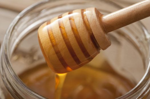 Close up on a wooden honey dipper coated in honey held above an open honey jar