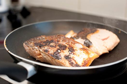 Fresh salmon steaks searing in the hot pan while preparing a healthy seafood dinner over the stove