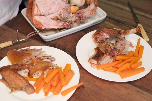 A close up of a rustic table setting with plates full of roast turkey and vegetables.