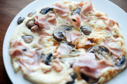 Delicious lightly fried serving of ham and mushroom omelette on a plain white plate for a healthy light snack or meal