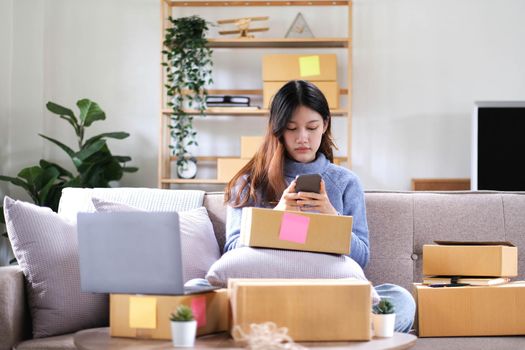 Business woman owner holding parcel box for delivery and using smartphone at home office. Entrepreneur small business working at home..