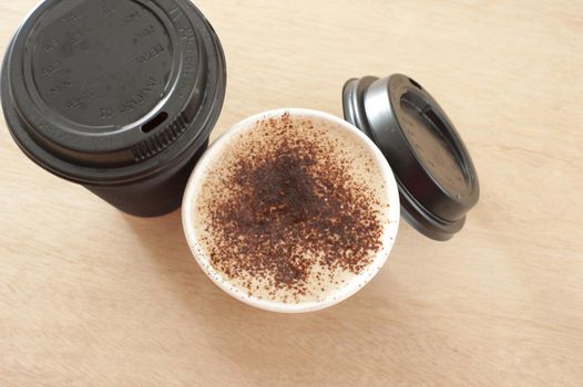 Two cups of freshly made frothy takeaway coffee in a disposable cup, one with the lid removed to reveal the beverage, on sealed, view from above