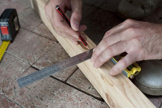 Man marking a square for a right angle cut on a plank of wood in his woodworking workshop as he renovates his home