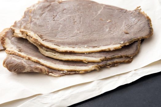 Sliced roast beef in close-up on white paper on kitchen table