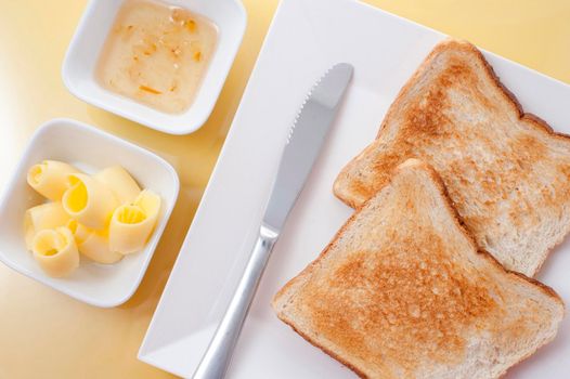 Overhead view of two slices of white toast served with butter coils and marmalade on the side for breakfast