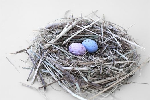 Small nest of straw with two pastel coloured candy Easter Eggs on a white background