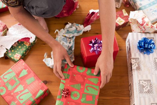 A close up of a teenager unwrapping Christmas presents on a timber floor.