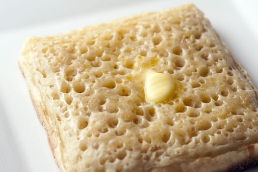 Extreme close up of buttered crumpet with numerous air holes on a white plate