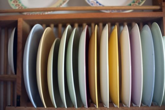 Wooden rack mounted on a wall with assorted colorful plates standing upright in a kitchen in a close up view
