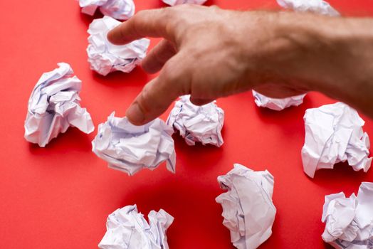 Human hand throwing away balls of paper against red background