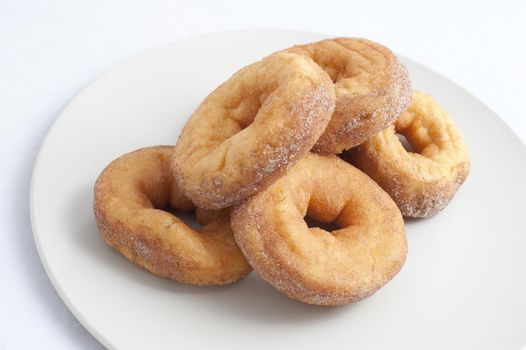 Plate of fresh ring donuts or doughnuts sprinkled with sugar for an unhealthy, but tasty, breakfast