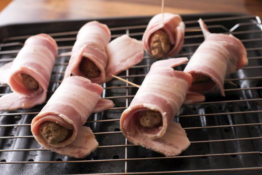 Uncooked bacon rolls or pigs in blankets with rashers of bacon around pork sausages ready on the grill for cooking