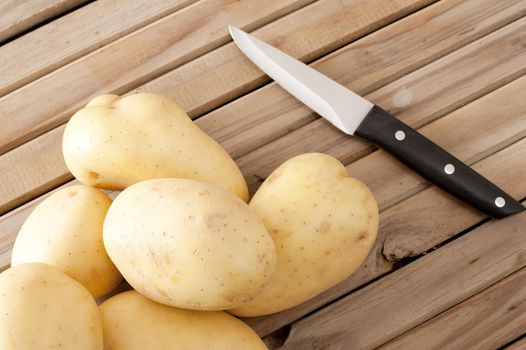 A close up of white potatoes and a sharp knife on a timber slatted bench.