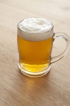 Tankard of golden draught beer with a frothy head on a wooden table or bar counter, symbolic of the Oktoberfest