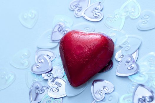A single, red valentine chocolate on metallic wedding heart confetti decorations.