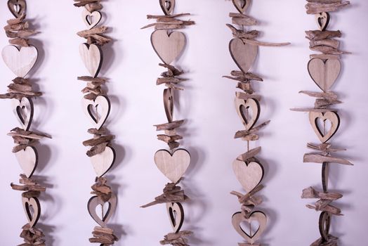 Wooden colourless heart shapes strung on strings, hanging close to pink background as vertical lines. Background concept