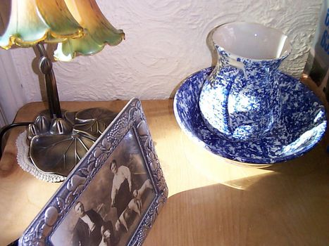Vintage decor with an old blue and white ewer and bowl, sepia family portrait and Art Nouveau style lamp standing on a wooden table top