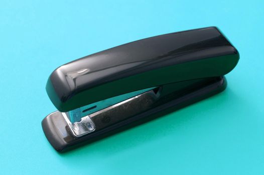 Close up Glossy Black Office Stapler Isolated on Blue Green Background
