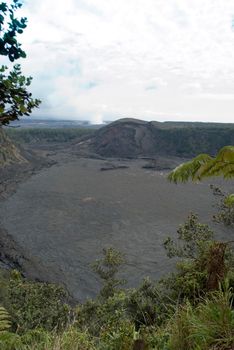 Solidified lava forms a flat surface in the Kilauea Iki Crater, Hawaii Volcanoes National Park, steam from the Kikauea Caldera crater can be seen to the rear