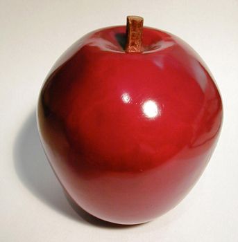 Close-up of a shiny red ceramic decorative apple, with shadow, on light grey background