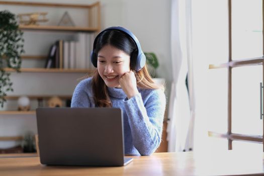 Cheerful beautiful Asian woman wearing headphones and look to digital tablet at video calling meeting and study online on the Internet..