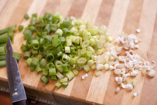 Chopped spring onion on wooden board with a knife