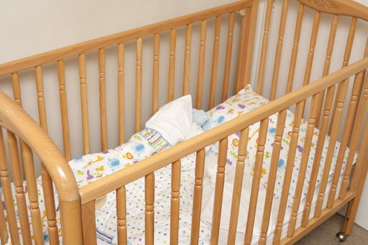 Empty wooden baby cot or crib with colorful pattern linen in the corner of a romom, close up view