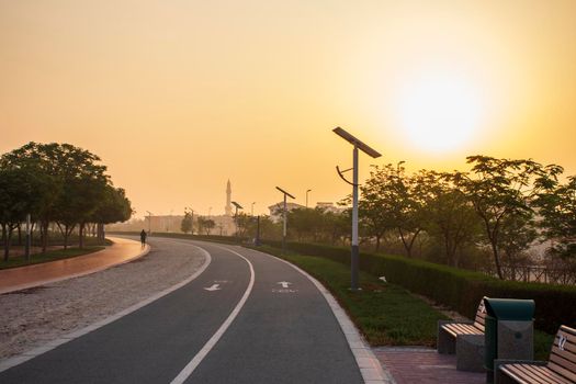 Jogging and cycling tracks in Al Warqa park, Dubai, UAE early in the morning. Lamp post powered by solar panels can be seen in the picture as well as minaret of a mosque. Outdoors