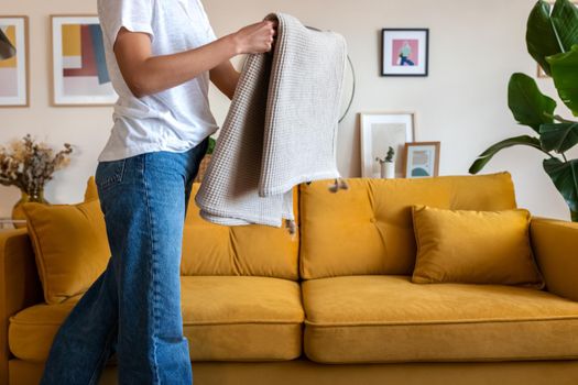 Unrecognisable woman folding blanket tying up living room, cleaning the house. Lifestyle concept.