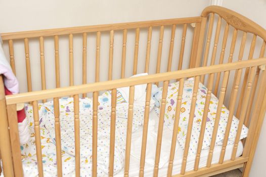 Empty pine colored wooden baby crib with folded over blanket in corner of room
